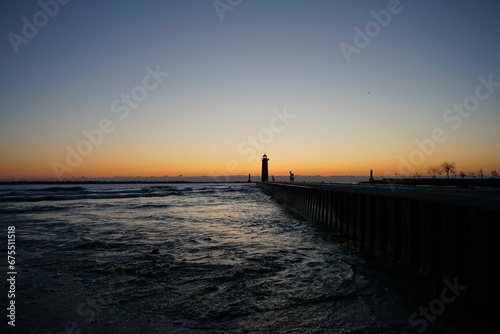 the sun is setting behind a lighthouse on the water near shore