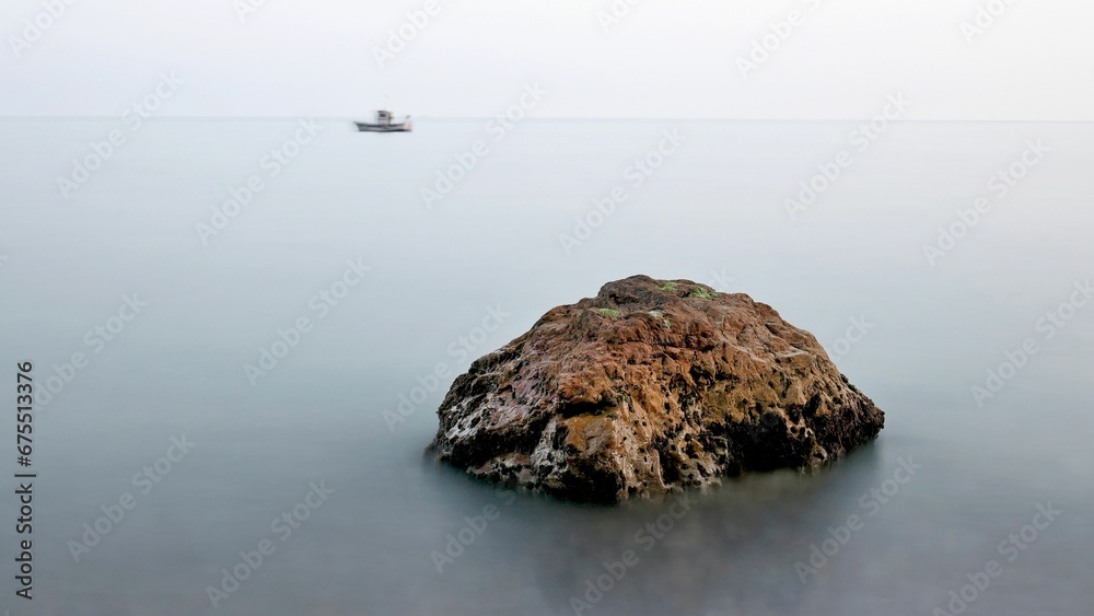 Solitary rock jutting out of the ocean, with a sailboat resting upon its surface Solitary rock jutting out of the ocean, with a sailboat resting upon its surface