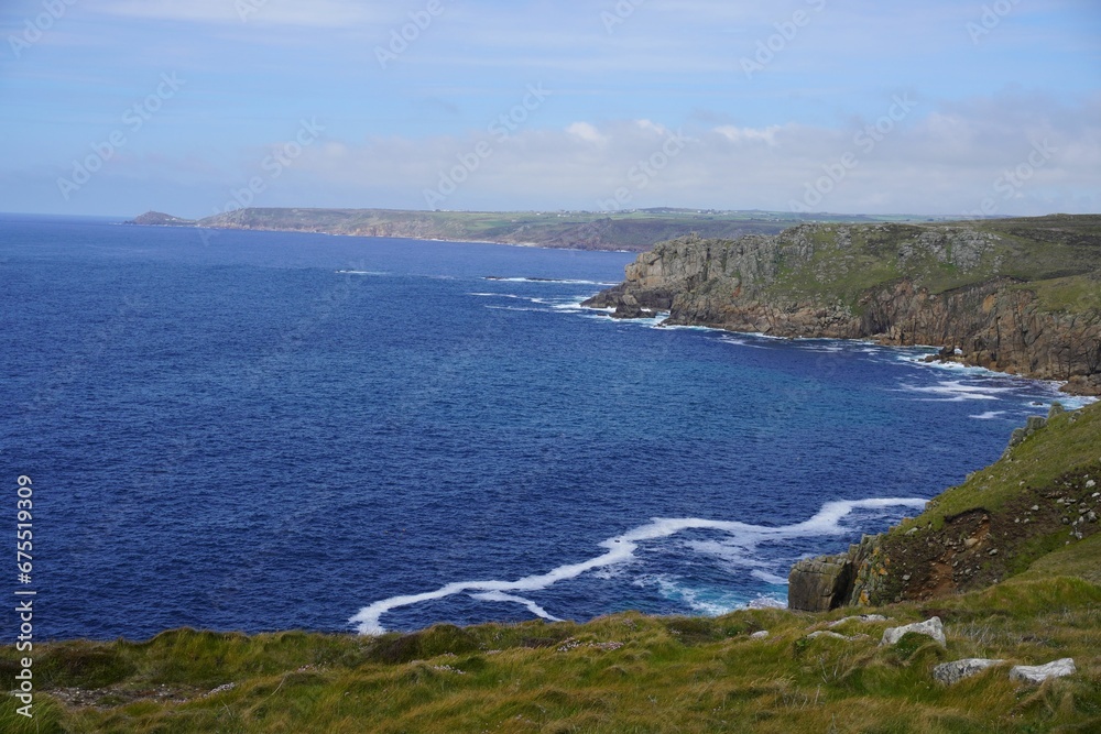Landscape of the sea surrounded by cliffs and greenery under a blue cloudy sky