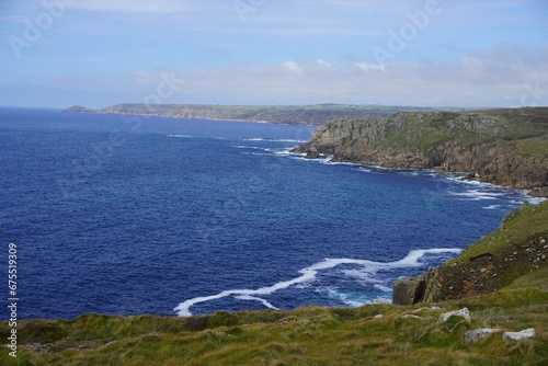 Landscape of the sea surrounded by cliffs and greenery under a blue cloudy sky