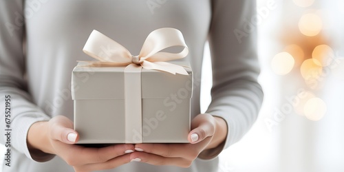 Woman hands holding a luxury white silver gift box with bow against a festive background, Xmas and New Year postcard design. Black Friday sales, Birthday celebration party concept