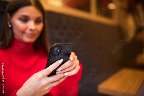 Woman in red sweater checking e-mail in social network via mobile phone while sitting near copy space for promotional content. Female online banking via smartphone gadget