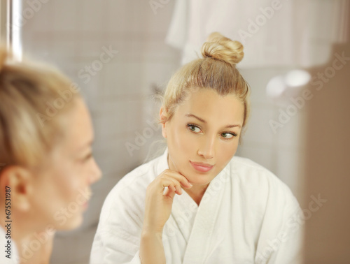 woman looking in the mirror in the bathroom and taking care of her skin.