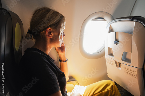 Passenger woman is flying in plane. Girl sitting in airplane looking out window going on trip vacation travel. Traveling female inside plane enjoying flight. Traveling girl