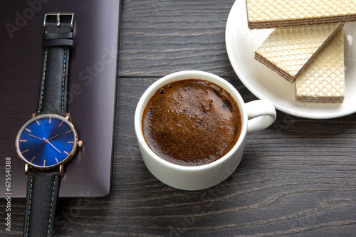 white cup of black coffee with cookies on the office table next to the laptop and clock. business and breakfast time.