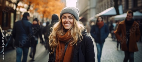 A happy woman is pictured in a black winter coat as she walks down a city street embodying the hipster lifestyle and enjoying her autumn vacation surrounded by people of different background