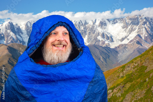 Happy bearded man in a sleeping bag against the backdrop of nature in the mountains. nature hikes in the mountains