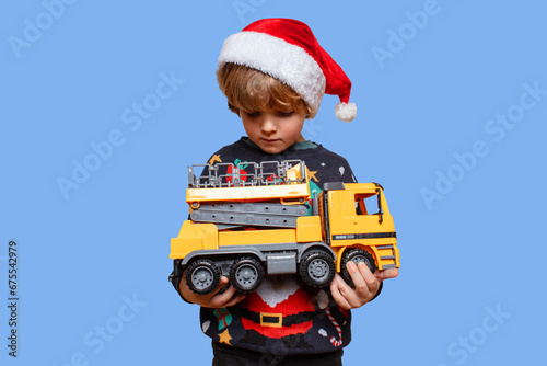 Christmas boy in a holiday clothes. Happy child on a blue background with a Christmas toy car. Boy have Christmas surprise. Happy New Year. Merry Christmas!