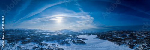 Fototapeta Naklejka Na Ścianę i Meble -  Very wide scenic aerial panorama on frozen lake, mountains with snow mobile traces, sunny blue sky with arched plane traces, contrails. Scandinavian white winter landscape, Norway, Sweden