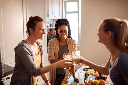Young female friends drinking fresh juice from vegetables in the kitchen photo