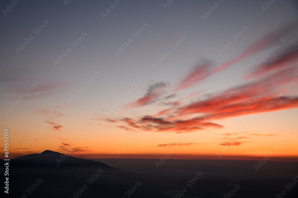 Majestic view of silhouettes of mountains and low clouds at colorful sunset.