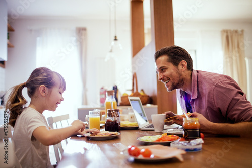 Happy little girl having breakfast with her father in the kitchen