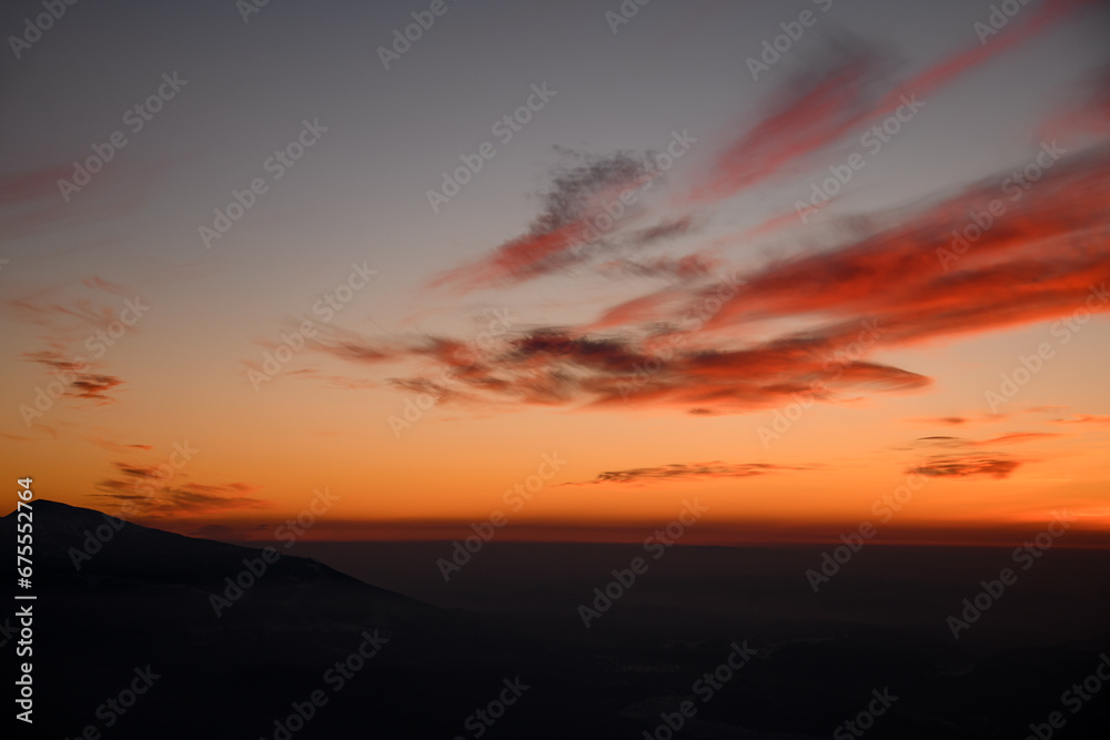 Beautiful scene of winter mountains surrounded by fog and bright clouds during twilight