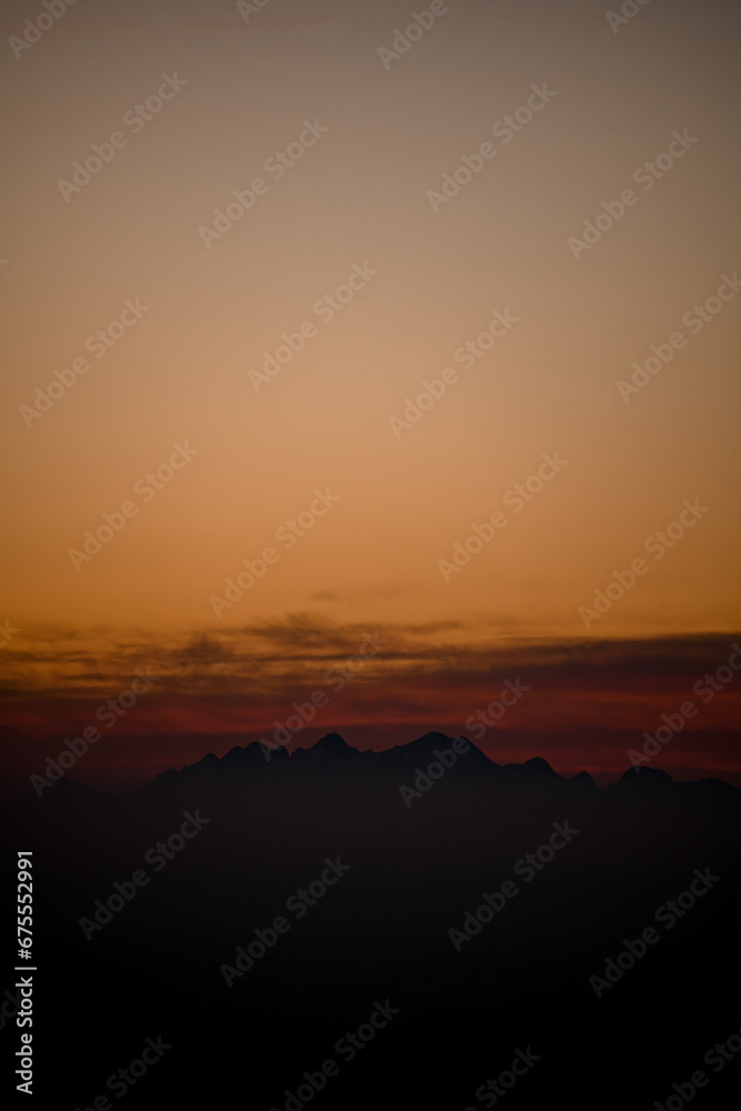 View of silhouettes of mountains and low colorful clouds at sunset.