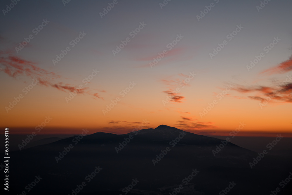 Colorful sunset over mountain peak silhouette surrounded by low weightless clouds