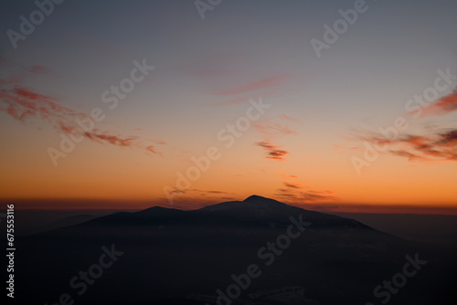 Colorful sunset over mountain peak silhouette surrounded by low weightless clouds