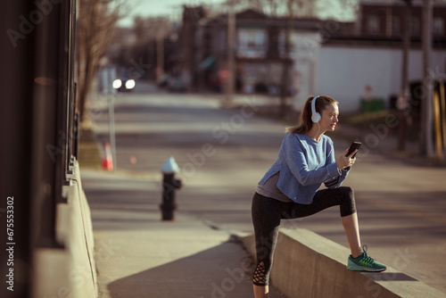 Young fitness woman holding smartphone and stretching before jog outside
