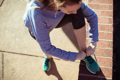 Young woman runner tying her sneakers on the sidewalk