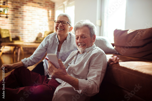 Senior couple laughing using smartphone together at home