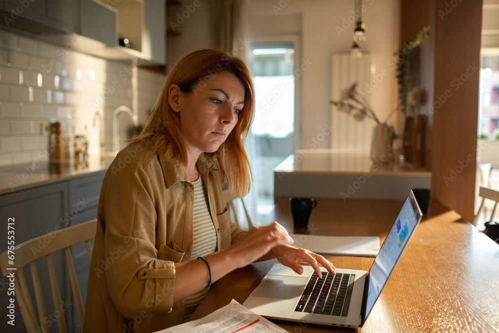 Serious woman sitting at desk typing laptop at home Serious woman sitting at desk typing laptop at home