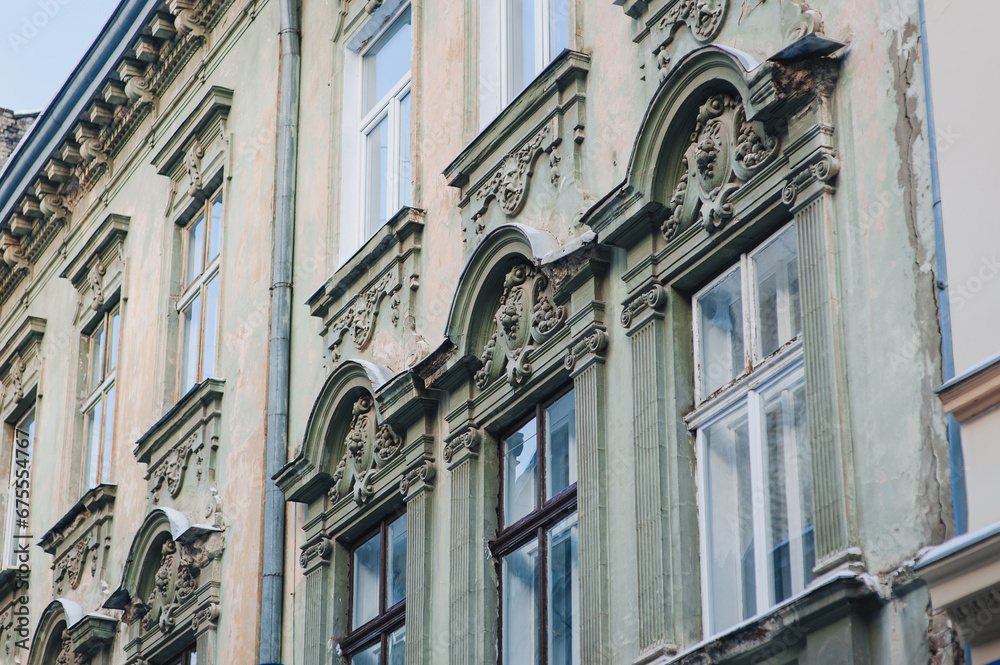 Fototapeta premium Windows with wooden frame. Neoclassical building with sandriks, porticoes and mascarons in the form of plant reliefs and head sculptures. Green and beige facade of an old house in Lviv, Ukraine.