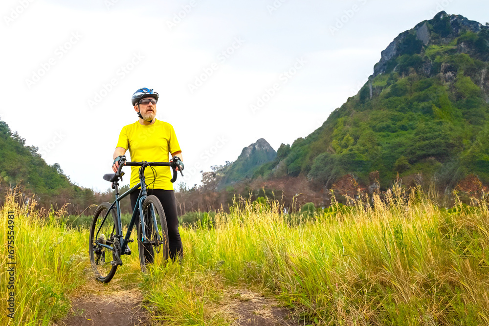 Obraz premium bearded man cyclist in yellow clothes rides a bike on a road in nature. sports, hobbies and entertainment for health