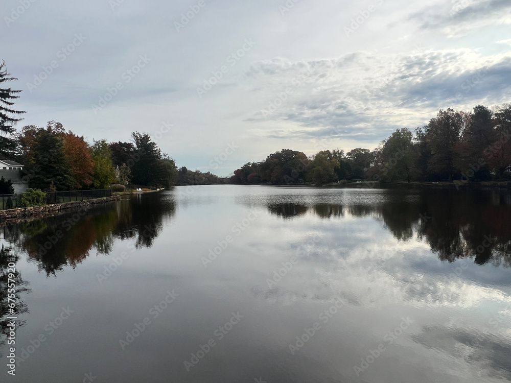 View of the Brainerd Lake in autumn in Cranbury, New Jersey, United States. Autumn landscape with lake, trees and cloudy sky reflected in water