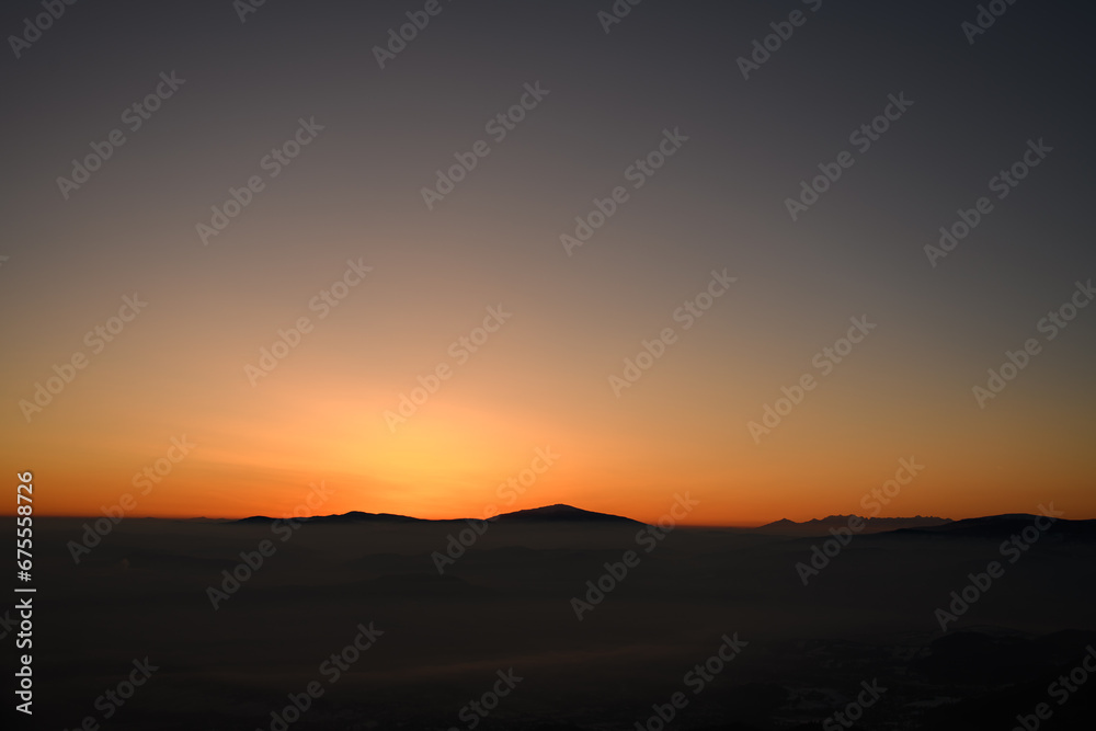 Panoramic view during sunset over snow cladded mountain peaks covered with smoky fog