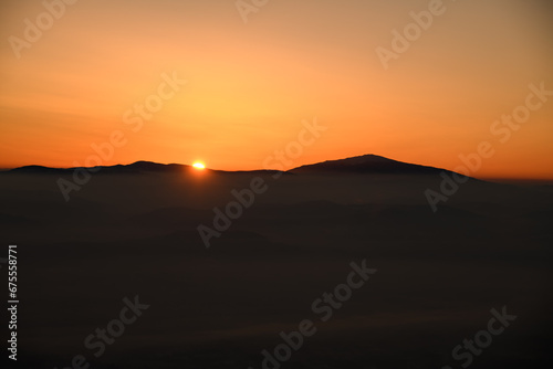 Mesmerizing view of the sun setting behind sharp mountain peaks shrouded in mist
