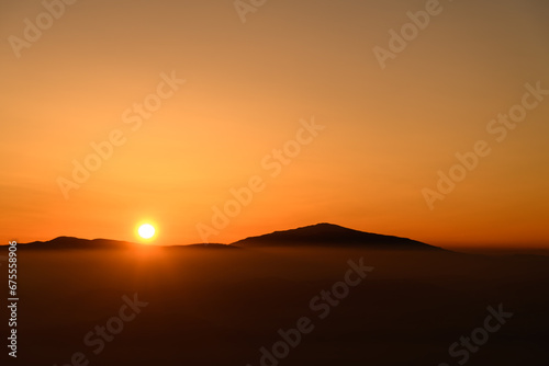 Amazing view of the sun setting behind sharp mountain peaks shrouded in mist