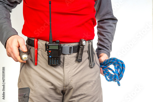 Pen, walkie-talkie, knife and flashlight with clips on the waistband of trekking pants. EDC items