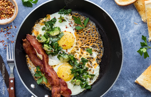A close look into a fry pan of cheddar fried eggs with a herb salad and bacon.