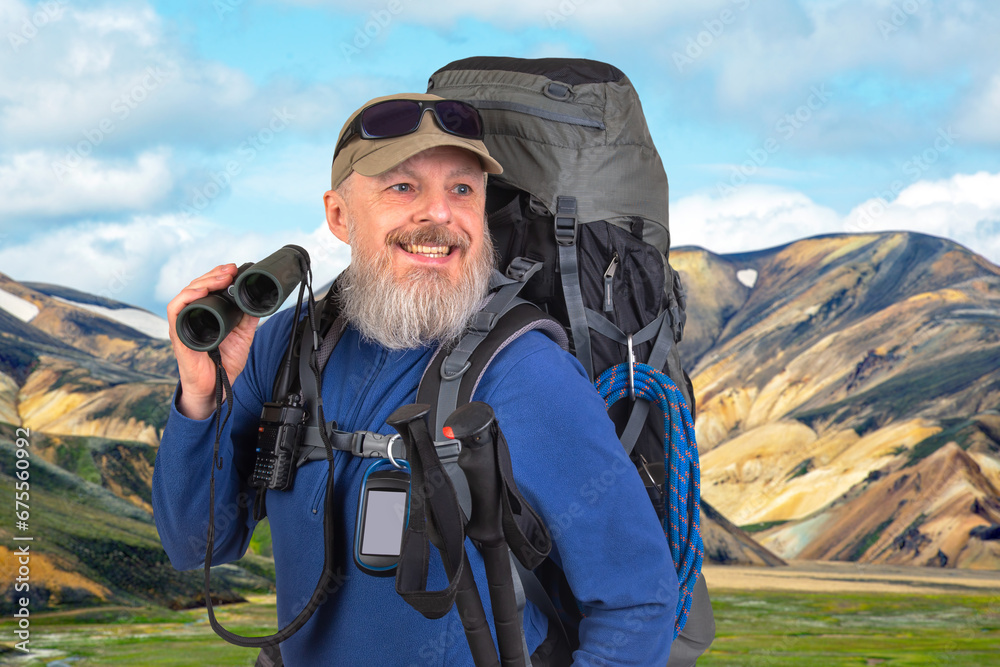 bearded man traveler with tourist equipment and binoculars in hand against the backdrop of a mountain landscape