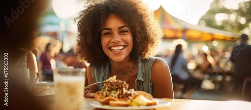 In the background of a vibrant outdoor setting a beautiful woman is surrounded by happy diverse people enjoying delicious food Among them a girl with a beaming smile holds a slice of white 