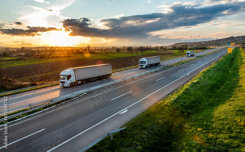 Highway transportation scene with Convoy of white transportation trucks in line on a rural highway at beautiful sunset