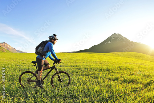 cyclist rides a bicycle on the green field towards the sun