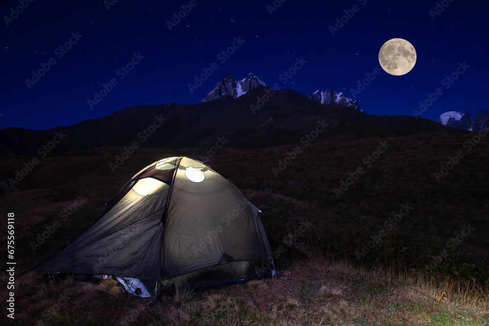 tourist tent at night in the mountains against the backdrop of the moon