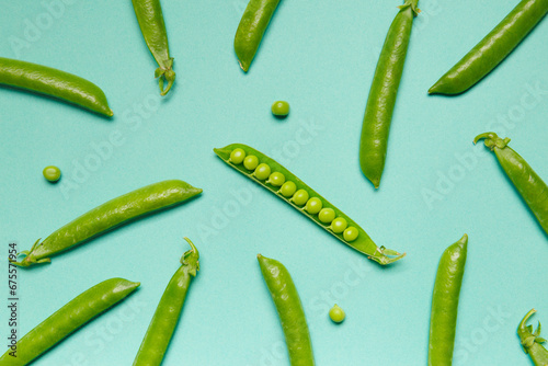 Fresh green peas in closed and open pods, pea grains are scattered on a green background, top view, studio photo.