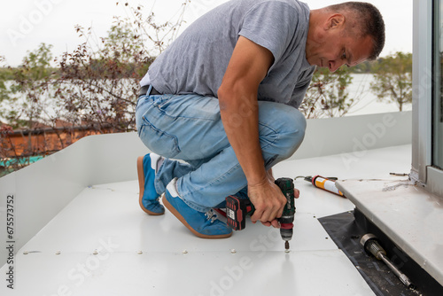 Construction worker installing new metal sheet roof. Man with cordless drill screws the roofing sheet to the roof of a  house. photo