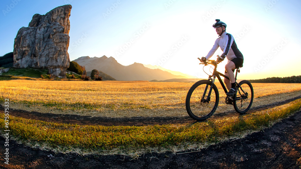 The cyclist rides a bike on the road near the field against the backdrop of the setting sun. Outdoor sports. Healthy lifestyle. The cyclist rides a bike on the road near the field against the backdrop of the setting sun. Outdoor sports. Healthy lifestyle.