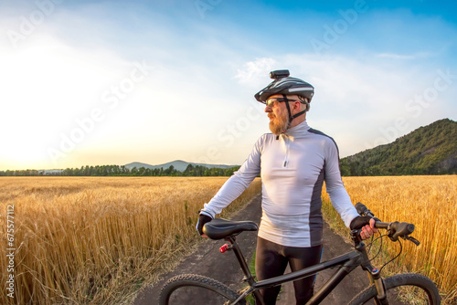 Fototapeta Naklejka Na Ścianę i Meble -  the cyclist with the bike in a field watching the sunset. sports and hobbies. outdoor activities