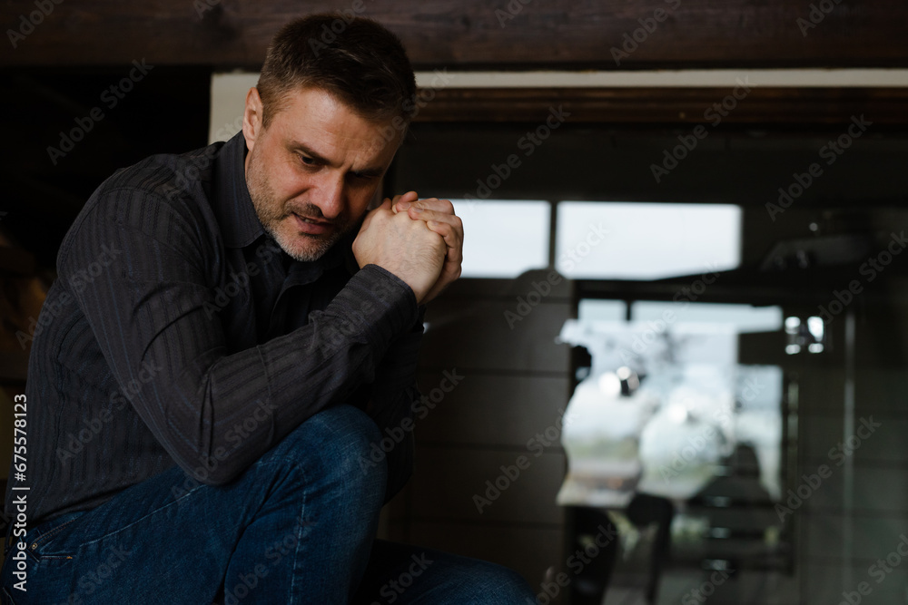 Alone man sitting at home in depression. Stressed male clasped arms begging god help with problems. Adult daddy praying for his family wellbeing. Human asking jesus christ support Alone man sitting at home in depression. Stressed male clasped arms begging god help with problems. Adult daddy praying for his family wellbeing. Human asking jesus christ support