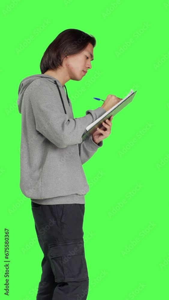 Profile of young man taking notes and thinking about ideas to write on clipboard papers, using files for inspiration in studio. Adult being thoughtful and in doubt, writing information on camera.