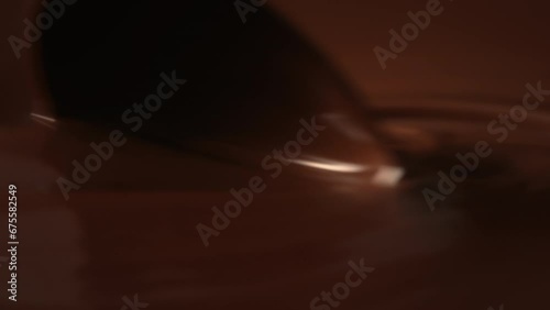 Close-up stirring melted chocolate with pastry spoon, hot liquid chocolate in bowl, mixing molten milk chocolate fondue. Cooking handmade chocolate bars, dessert or candies. Confectionery slow motion