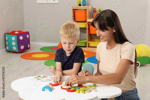 Motor skills development. Happy mother helping her son to play with colorful wooden arcs at white table in room