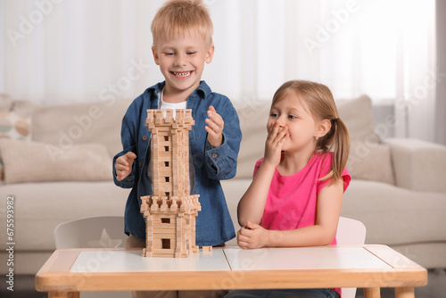 Little girl and boy playing with wooden tower at table indoors. Children's toy