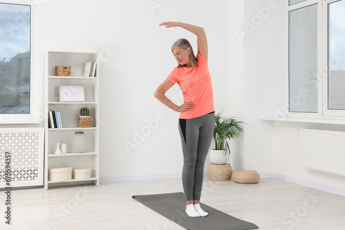 Senior woman in sportswear stretching at home, space for text