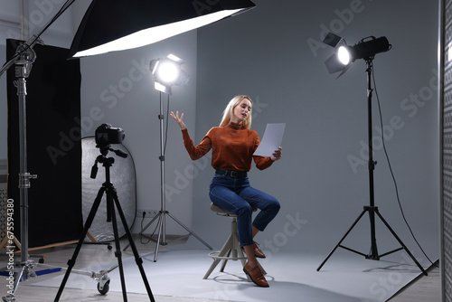 Casting call. Emotional woman with script sitting on chair and performing in front of camera in studio photo