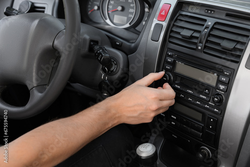 Listening to radio while driving. Man turning volume button on vehicle audio in car, closeup