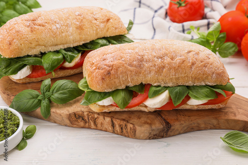 Delicious Caprese sandwiches with mozzarella, tomatoes and basil on white wooden table